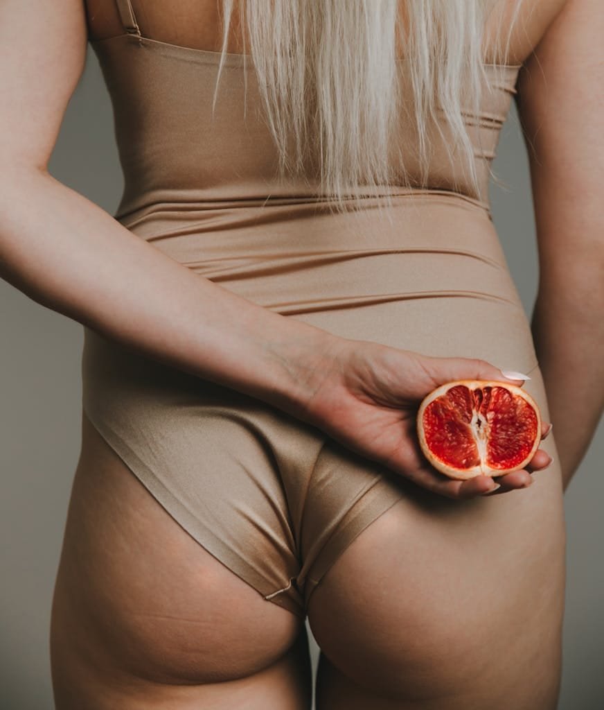 A woman's back view in a bodysuit holding a blood orange. Elegant and modern composition.